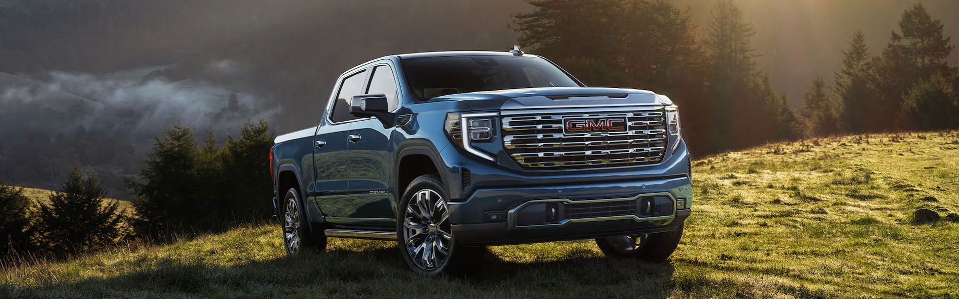 Black 2026 GMC Sierra 1500 parked in the middle of a forested mountain meadow