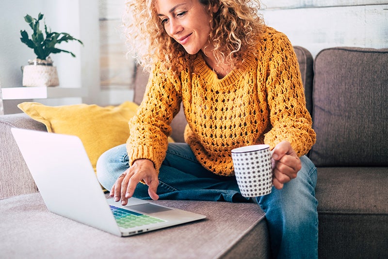 a lady is holding a cup of coffee and looking at something on her laptop